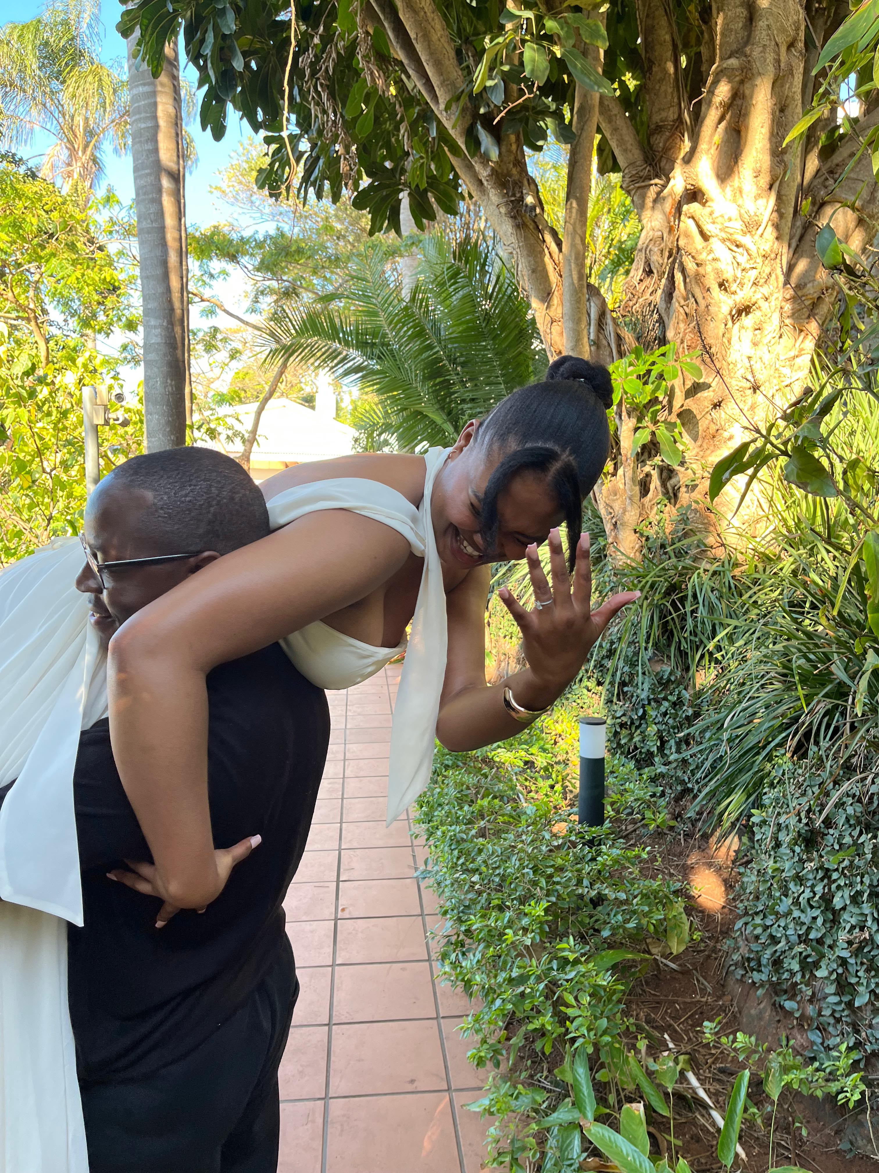 Ellen showing off her engagement ring while Chukwuma carries her piggyback in a garden