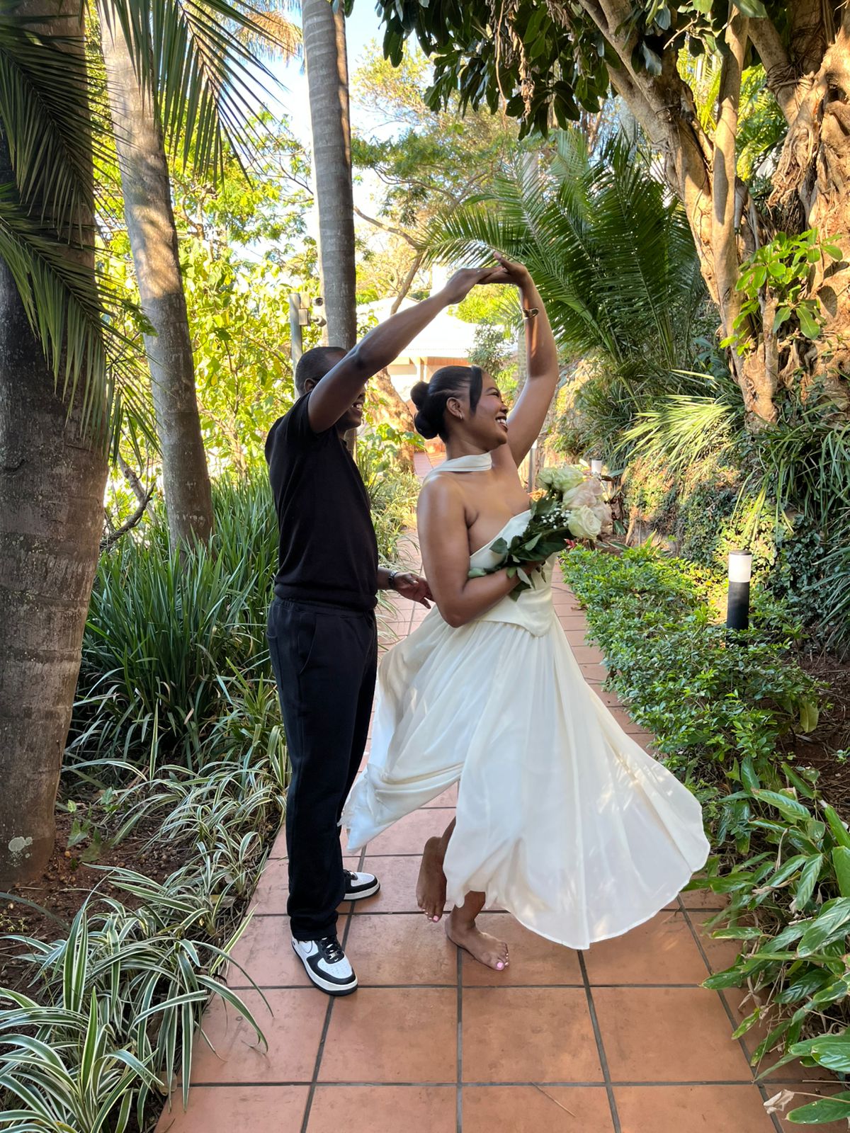 Chukwuma twirling Ellen as she dances in her wedding dress on a garden path
