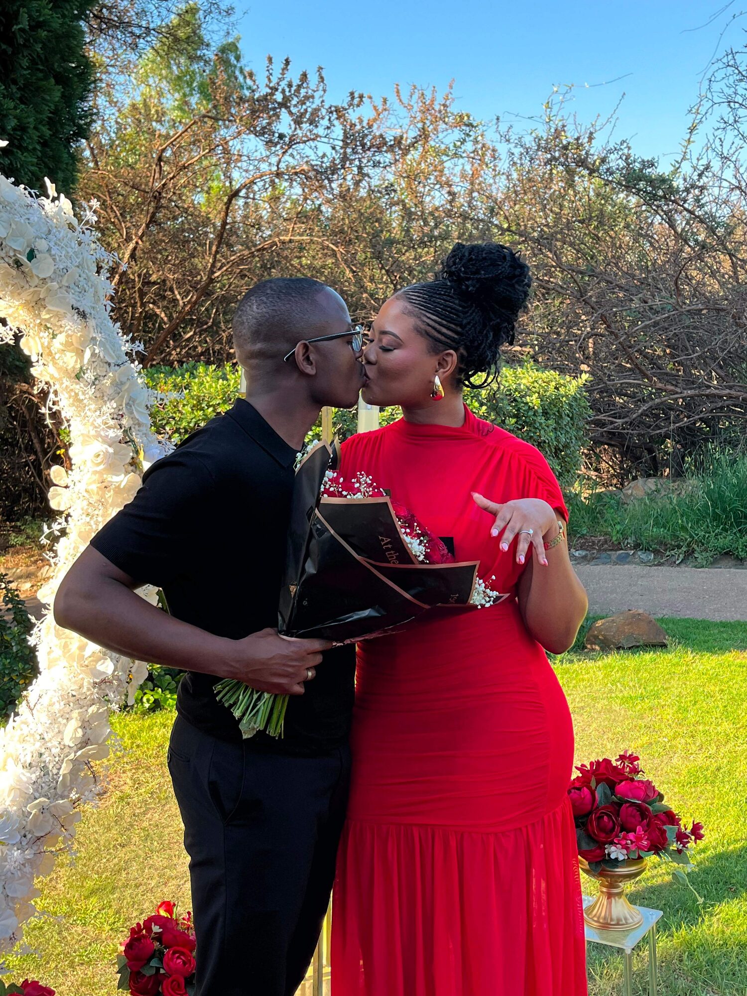 Chukwuma and Ellen kissing, holding a bouquet of roses
