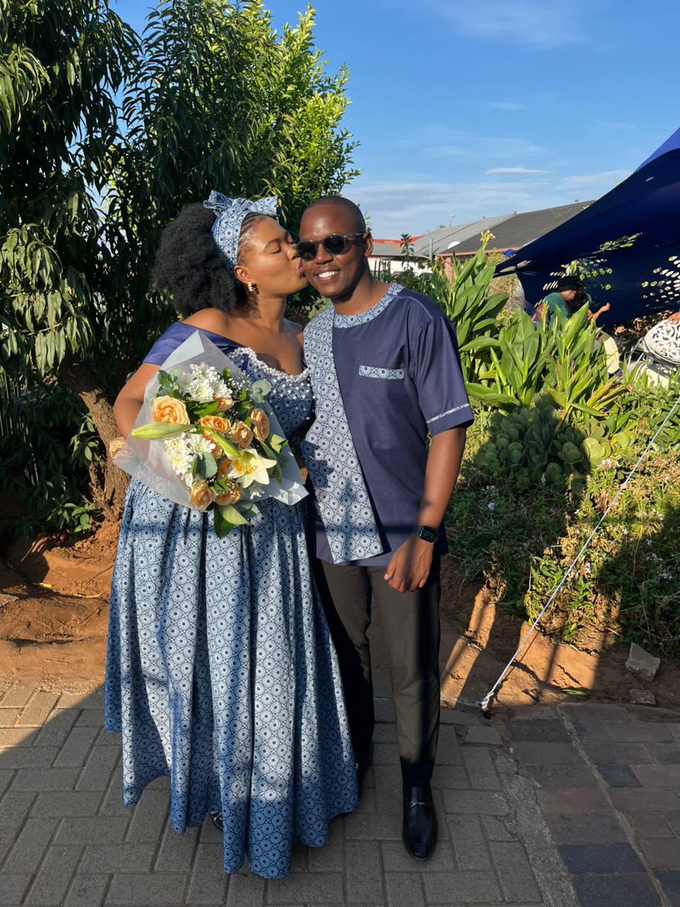 Chukwuma and Ellen sharing a kiss in matching traditional attire, Ellen holding a bouquet